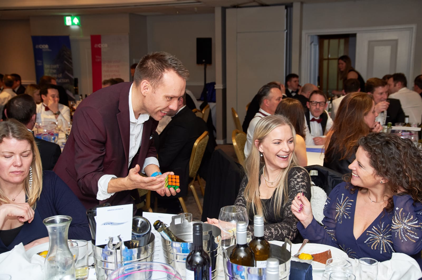 Guests laughing at a Rubik's cube routine during a black-tie dinner
