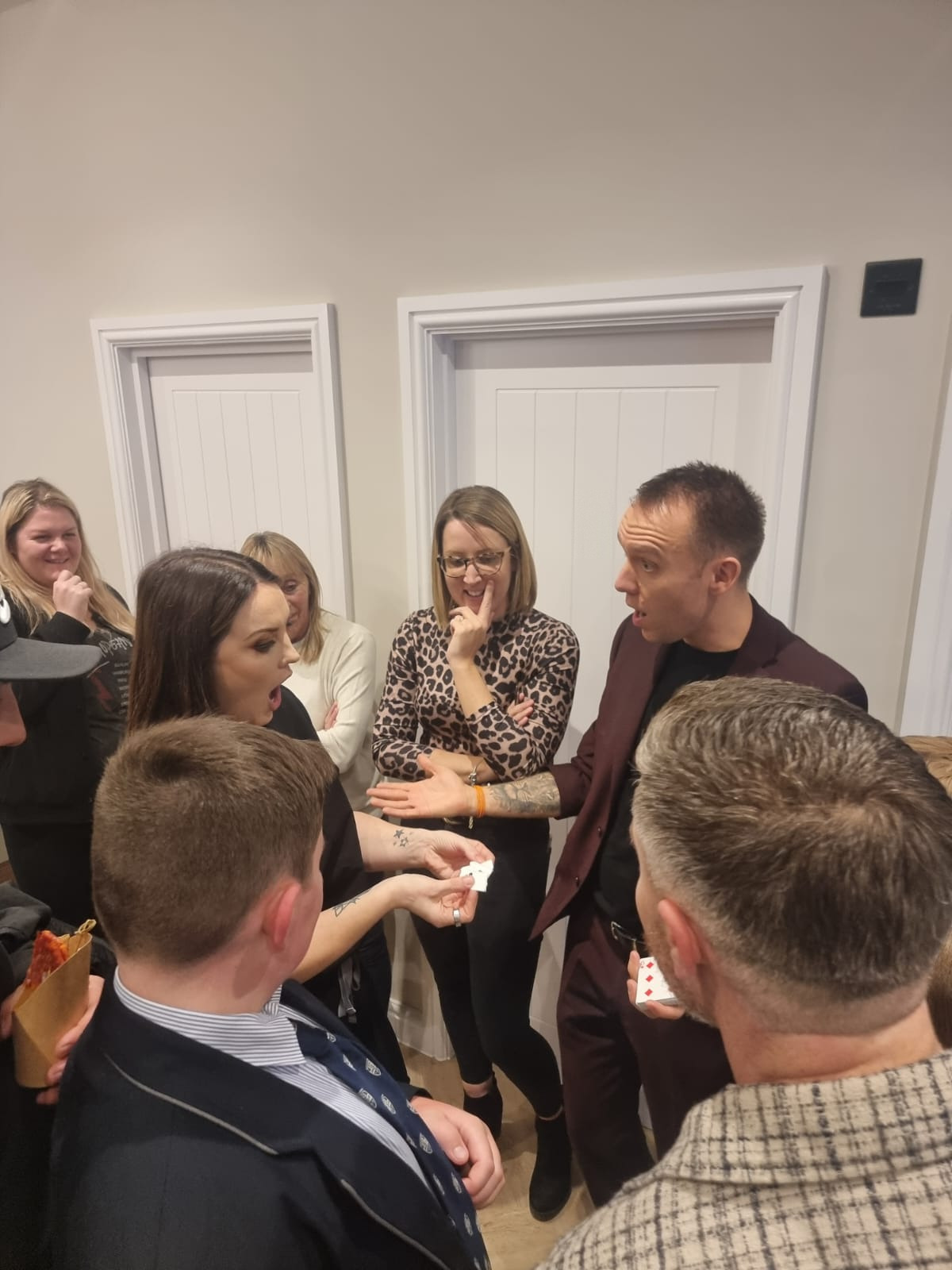 Standing guests reacting to a card reveal, drinks in hand