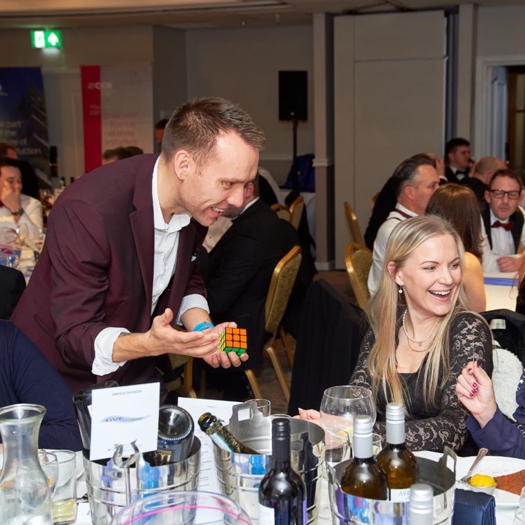 A guest laughing as Neil solves a Rubik's cube at a corporate dinner