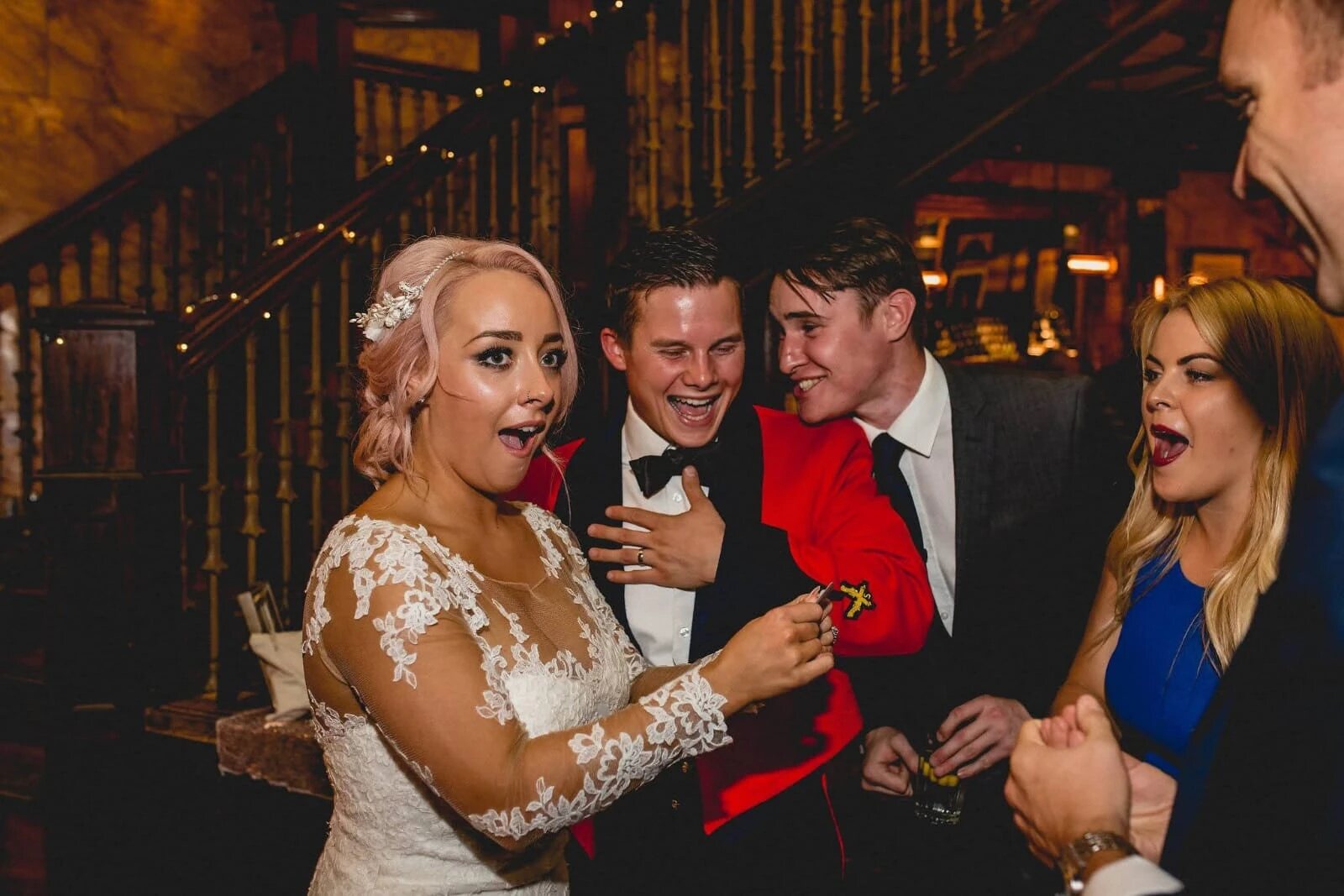 A bride, groom and guests open-mouthed in astonishment at a card reveal during their wedding reception